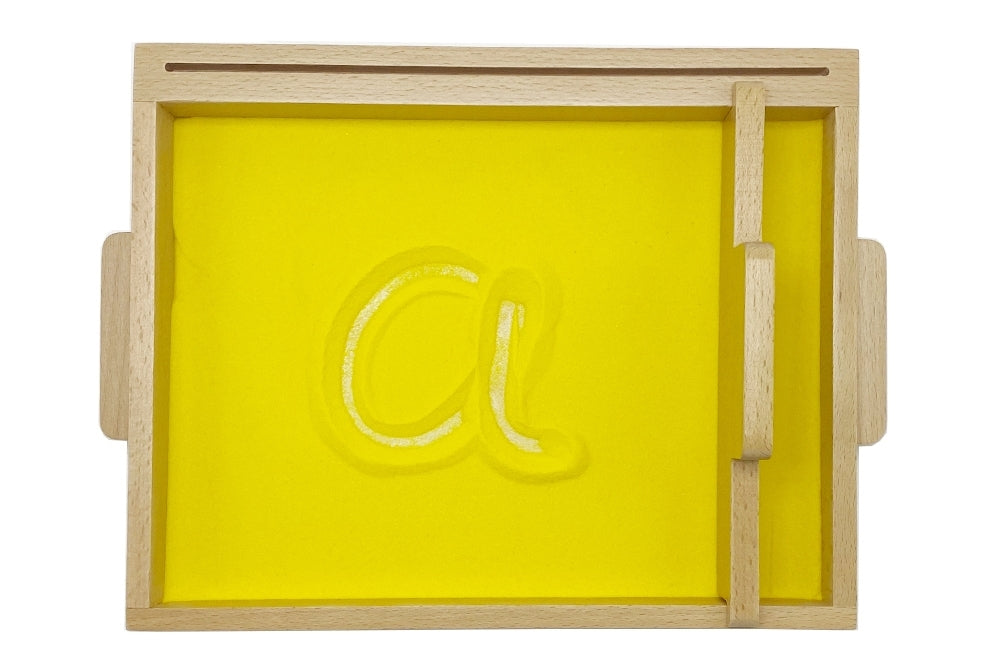 Sand tracing tray filled with yellow sand. The letter 'a' is traced into the sand.