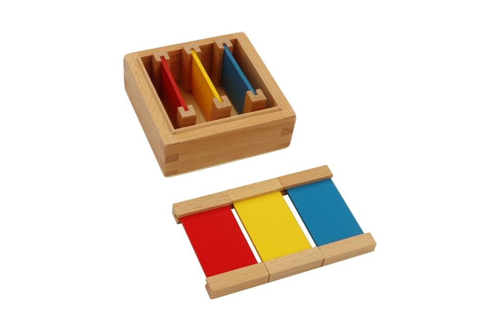 First colour tablet box. Small square box containing three pairs of tablets in the primary colours red, yellow, and blue. Three tablets are laid out in front of the box.